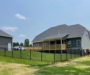A modern, multi-level wooden deck with stairs and railing, surrounded by lush vegetation and a clear blue sky.