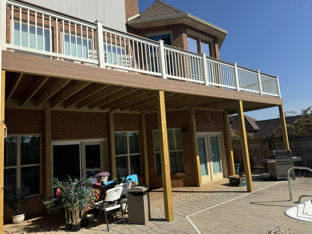 An elevated wooden deck and patio area with a brick chimney and multi-story house in the background.