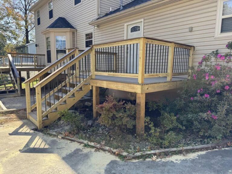 A wooden deck with stairs leading up to a house. The deck has a railing with a lattice pattern and is surrounded by a grassy area with plants.