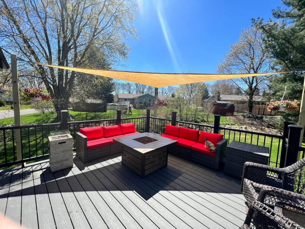 A covered patio with red patio furniture and a fire pit, overlooking a grassy yard with trees.