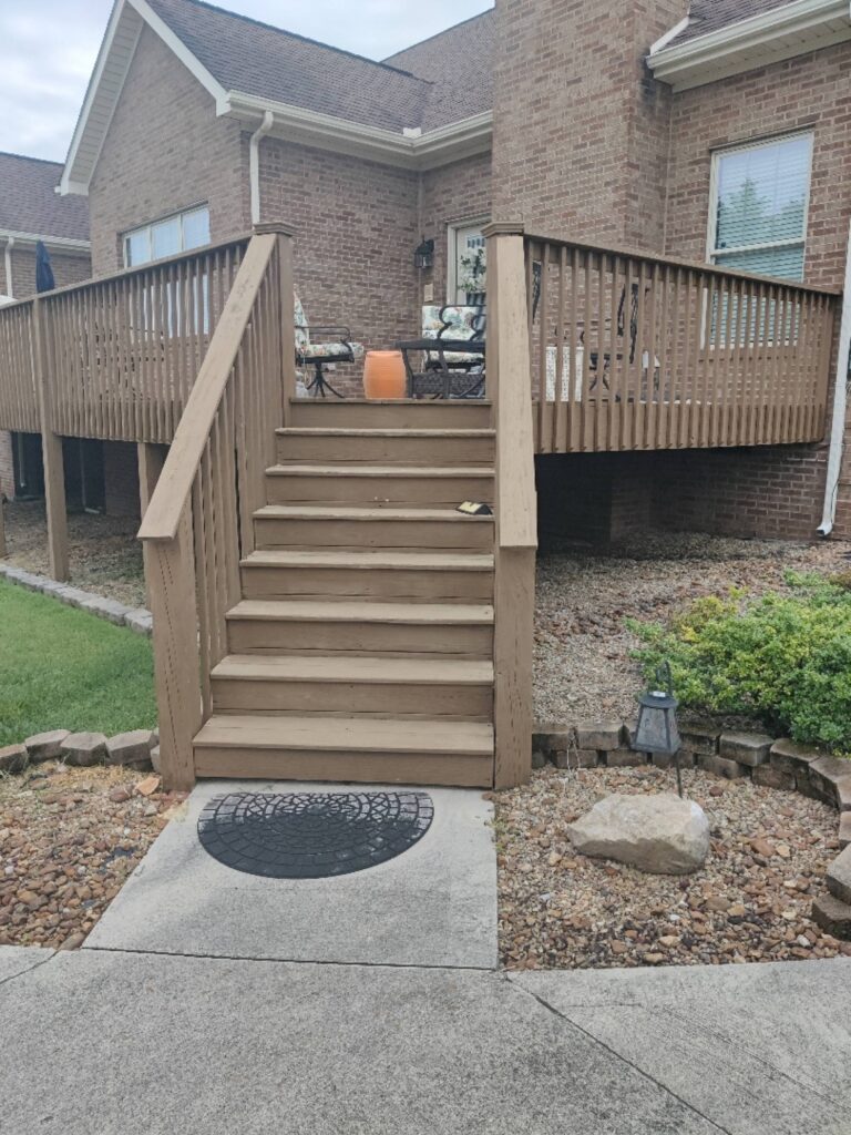 A close-up view of the wooden stairs and railing leading up to the deck of a two-story brick home.
