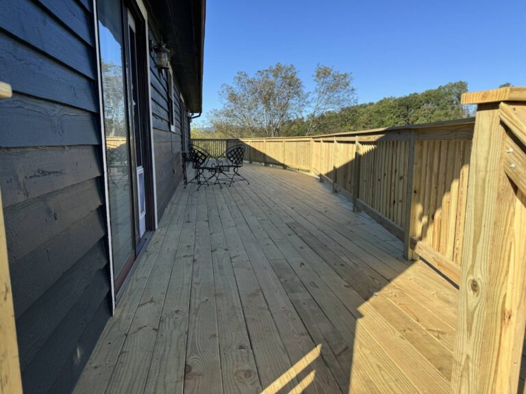A wooden deck with a railing overlooking a grassy yard and trees in the background.