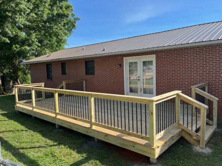 A wooden deck or porch with a railing system, built on an elevated platform and extending from the side of a brick residential building.