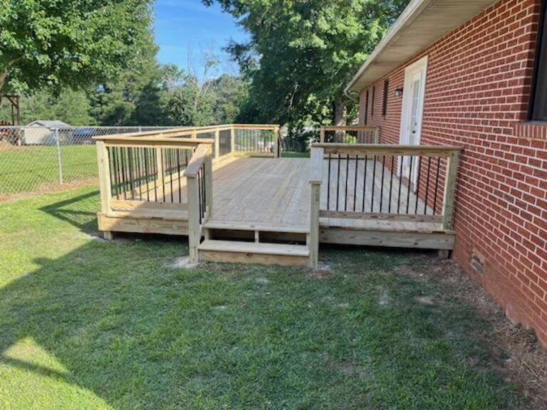 A wooden deck or porch with a railing system, built on an elevated platform and extending from the side of a brick residential building.