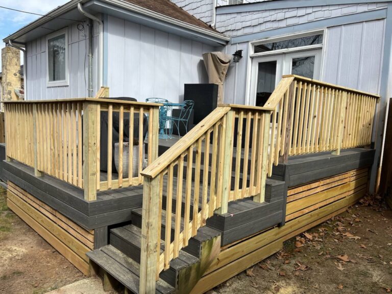 A wooden deck with railings and steps, attached to the side of a house with gray siding and a metal roof.