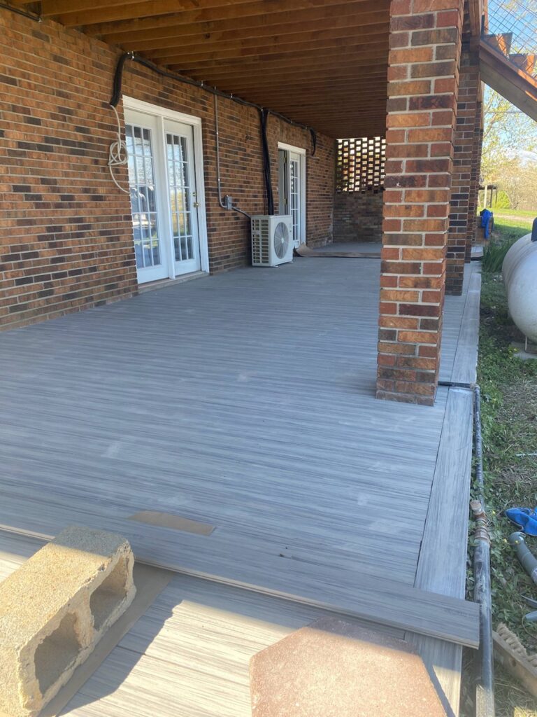 A covered porch with a wooden floor and brick walls, with various outdoor items and furnishings