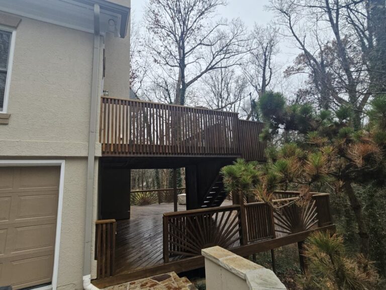 A two-story wooden house with a covered porch and a wooden deck with stairs leading down to the yard.